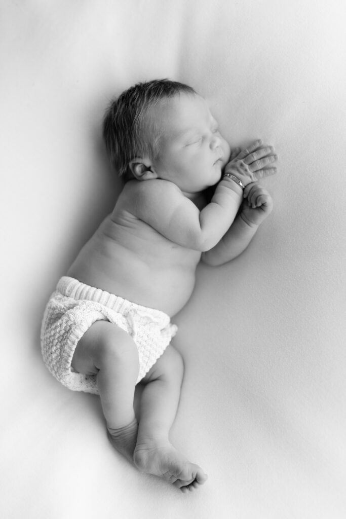 bovenaanzicht van newborn. met handjes langs het gezicht en een broekje van noppies aan.