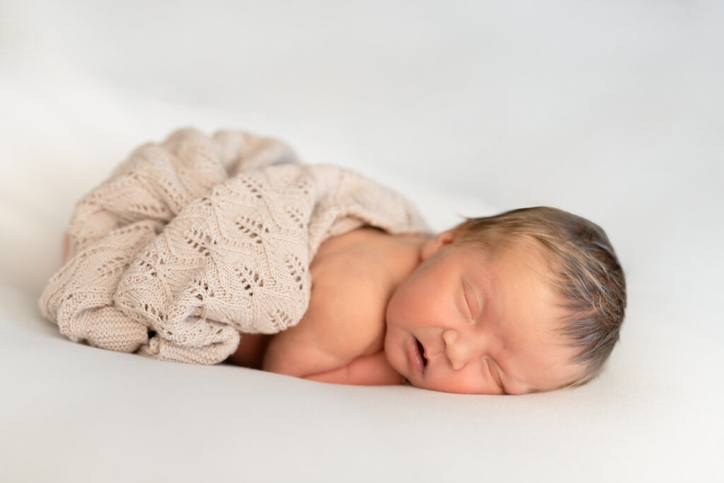 Vooraanzicht newborn met handjes onder dr hoofdje. met dekentje over zich heen.