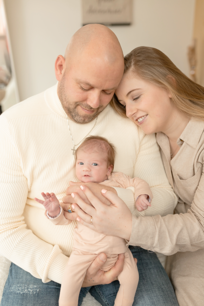 papa en mama houden de baby vast voor zich en knuffelen elkaar lief