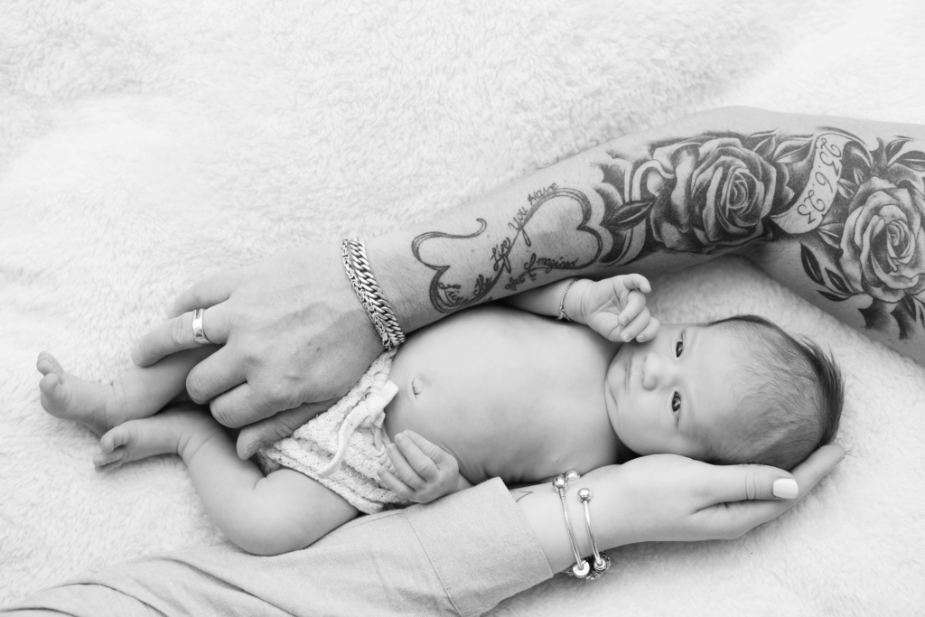 de newborn in de midden met de arm van papa en de arm van mama eromheen wat geborgenheid geeft