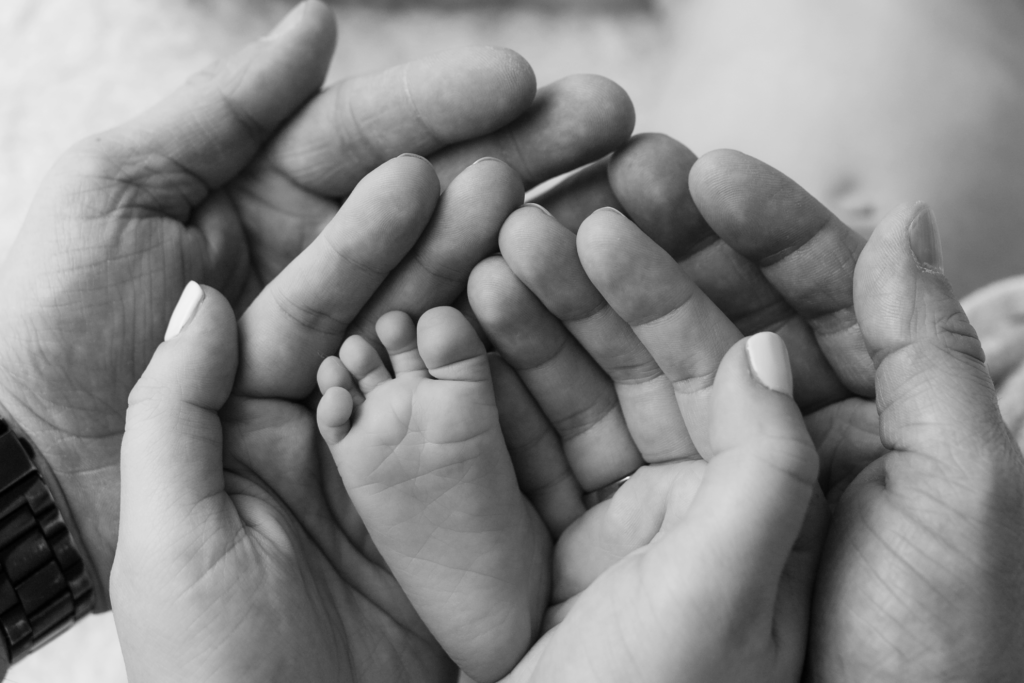 de handen van papa en mama met daarin de midden het voetje van de baby
