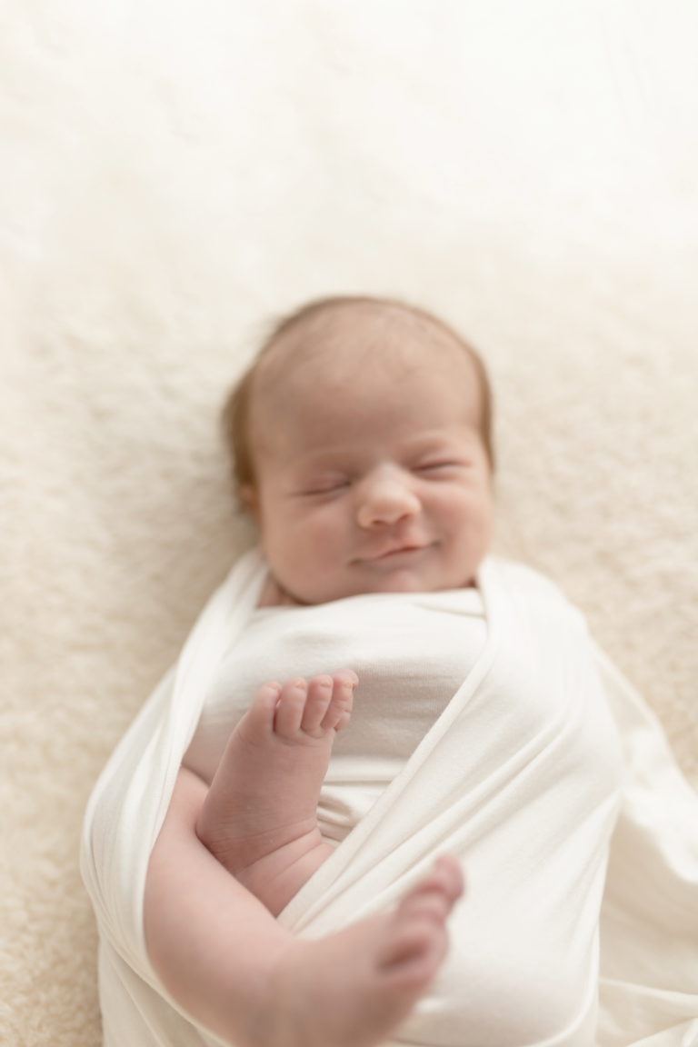 newborn vooraanzicht ingewrapt met voetjes naar buiten met een klein lache op haar gezicht
