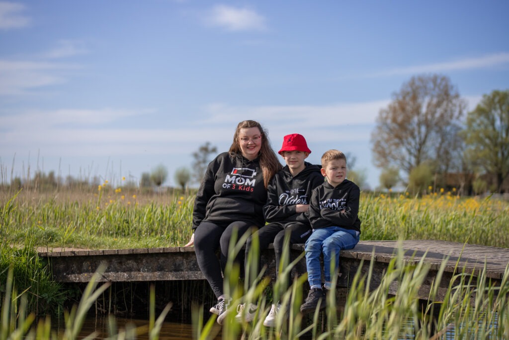 moeder zit met 2 van haar zoons op een bruggetje op een zonnige dag tijdens de familieshoot