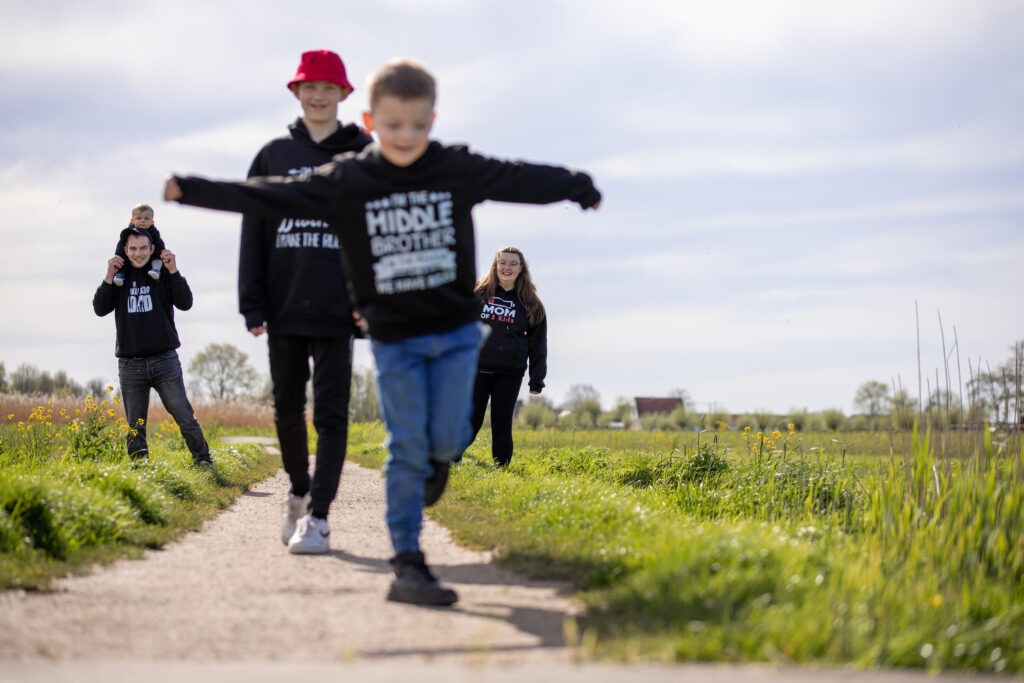 Familie loopt op pad. op een zonnige dag. middelste kind loopt voorop en ouders staan achterop in de rij