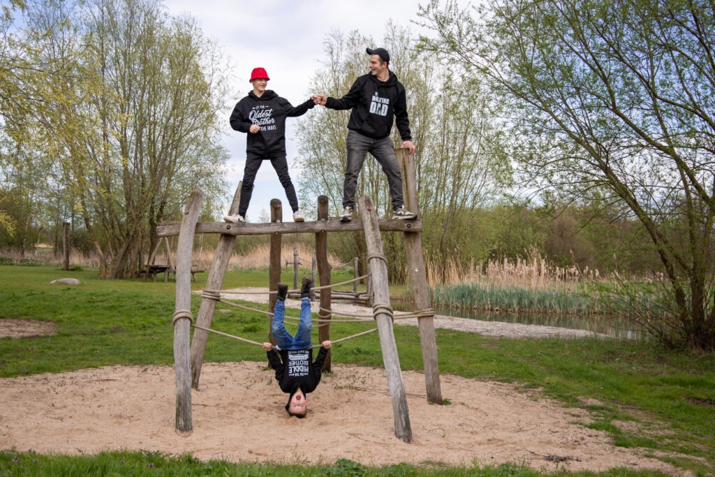 vader en zijn 2 oudste zoons op de foto vader en oudste zoon staan bovenop een speeltoestel en geven elkaar een box en dan middelste zoon hangt op zijn kop eronder