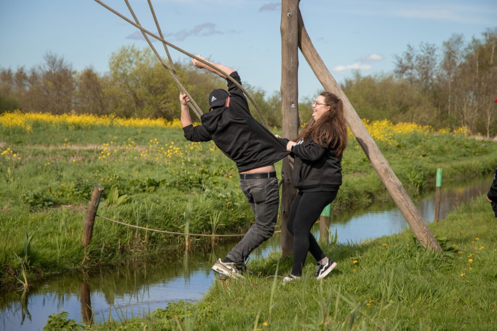 vader is in de touwen over het water geklommen en heeft de overkant bereikt moeder trekt hem aan zijn kleren om op het droge te krijgen in de natuurspeeltuin in Schiedam
