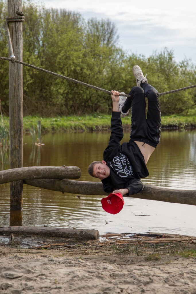 oudste zang hangt in de touwen boven het water en verliest zijn hoedje in het water en pakt deze eruit in de natuurspeeltuin in Schiedam