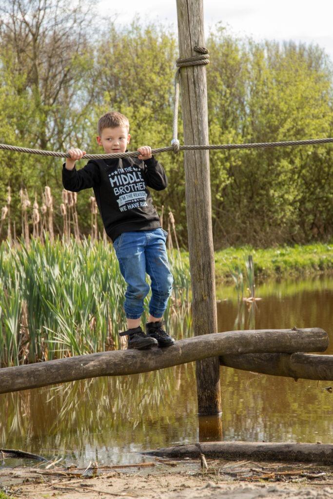 middelste zoon klimt over balk over het water in natuurspeeltuin in Schiedam