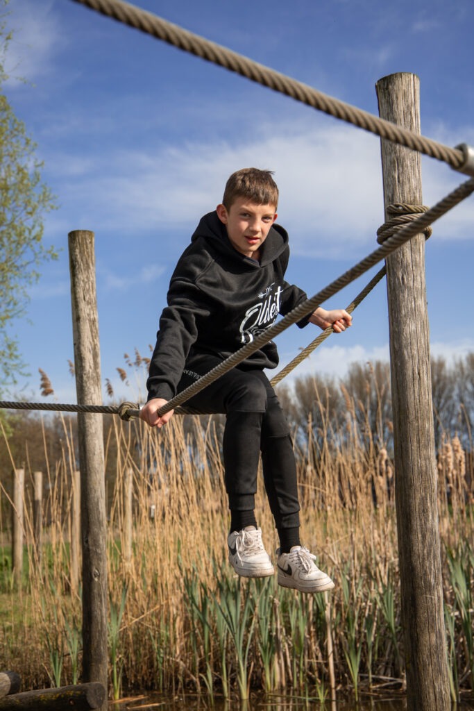 oudste zoon hangt in de touwen boven het water in de natuurspeeltuin in Schiedam