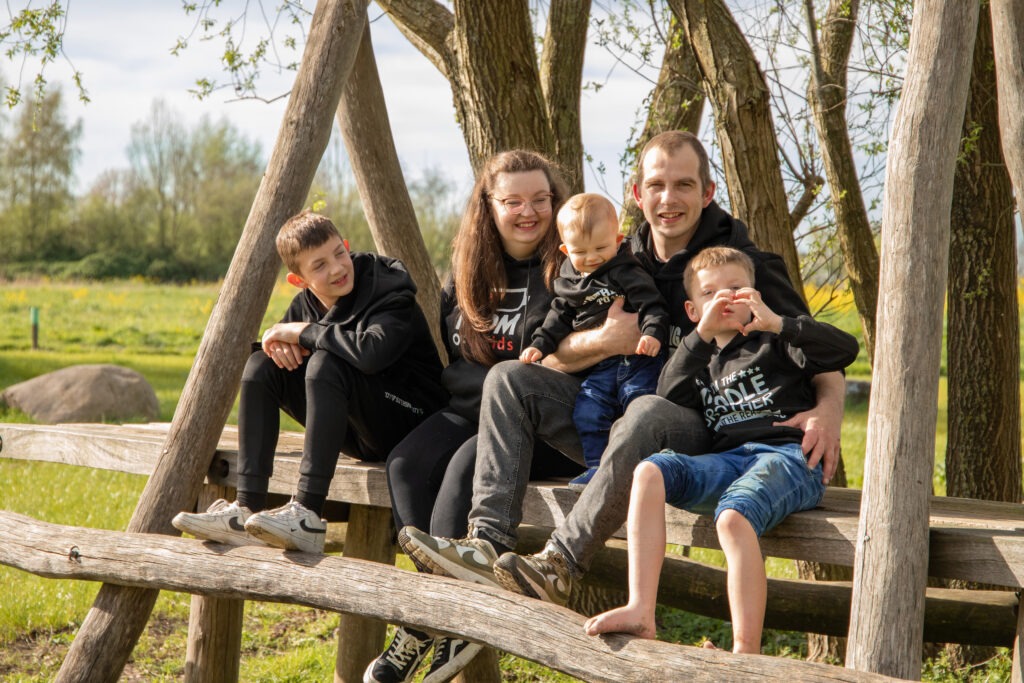 de hele familie zit op een speeltoestel en de middelste zoon maakt een hartje met zijn handen