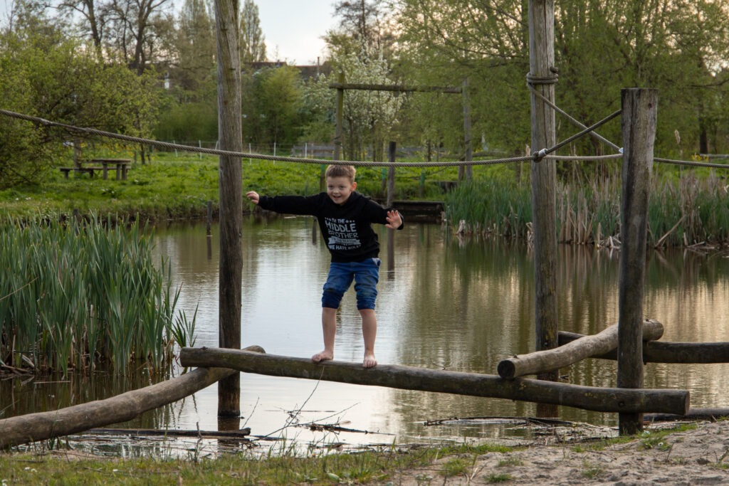 Kind staat op een balk boven het water in schiedam in de natuurspeeltuin