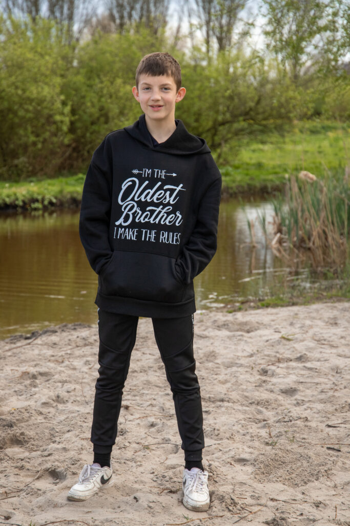 De oudste zoon staat alleen op de foto met een zwarte trui aan met daarop de tekst I'm the oldest brother i make the rules