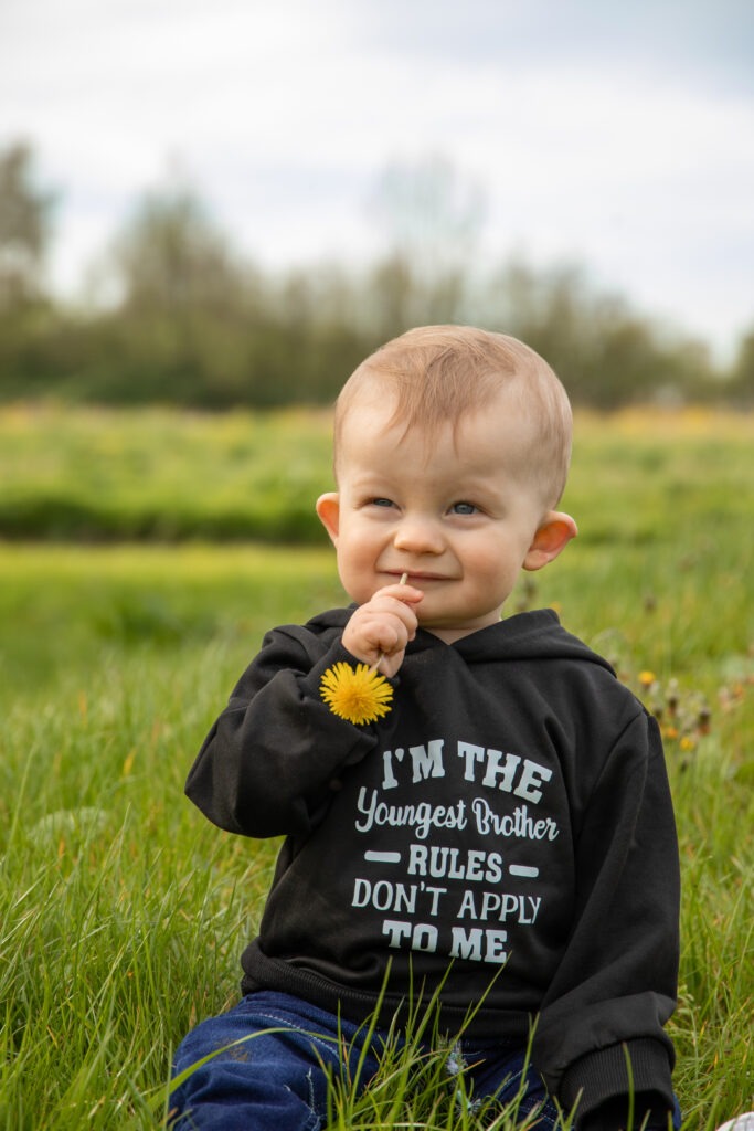 jongste zoon van het gezin zit in het gras met een paardenbloem in zijn mond in de natuurspeeltuin in schiedam