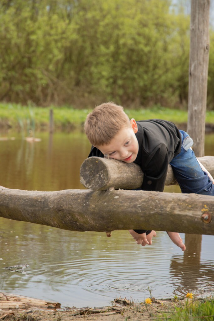 jongen ligt op een boomstam boven het water in de natuurspeeltuin in schiedam