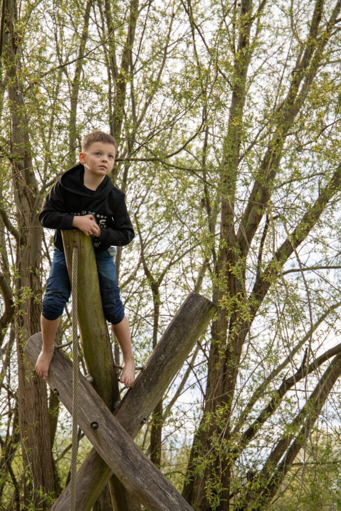 jongen in een klimtoestel geklommen in de natuurspeeltuin op zijn blote voeten