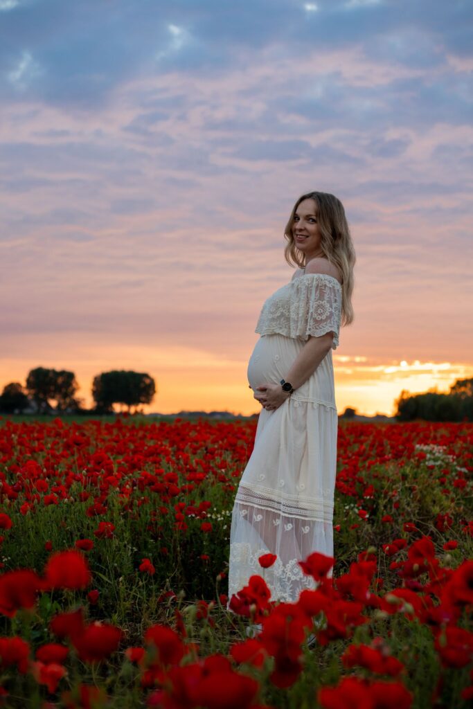 zwangere vrouw in creme jurk tijdens zonsondergang in een klaprozen veld