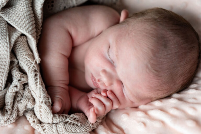 Zijaanzicht slapende baby met handje bij gezicht – De baby ligt op haar zij, met haar handje ontspannen tegen haar wang, terwijl ze diep slaapt op een pluizige ondergrond.