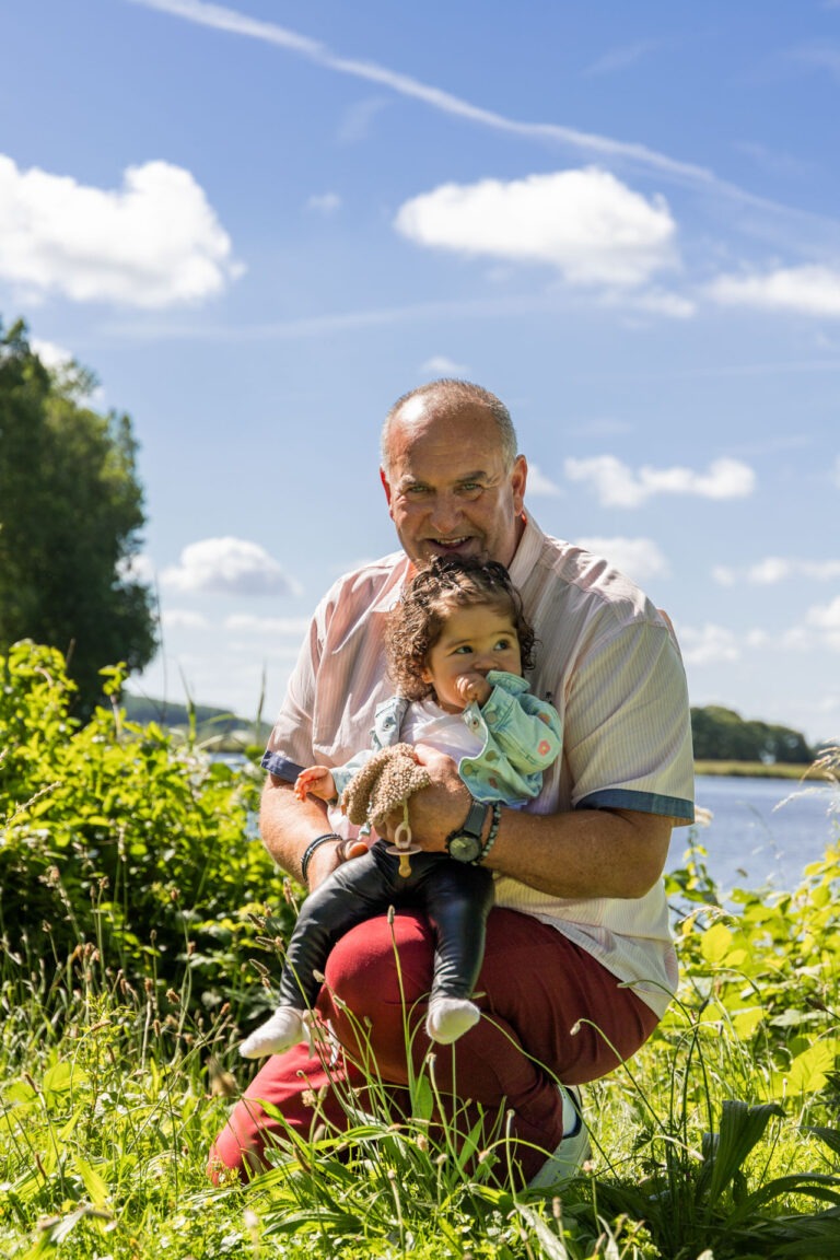 Opa houdt zijn kleindochter stevig vast, een dierbaar moment van verbondenheid tijdens de familyshoot buiten.