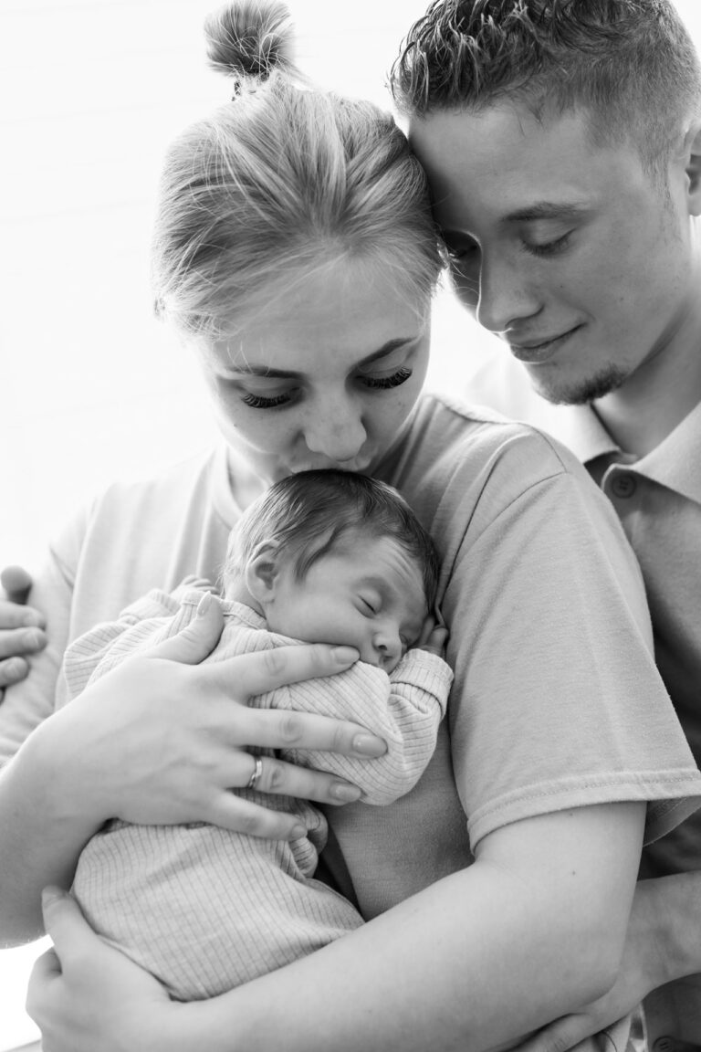 Een intiem familieportret in zwart-wit, papa en mama helemaal om hun slapende baby heen gevouwen – een cirkel van liefde.