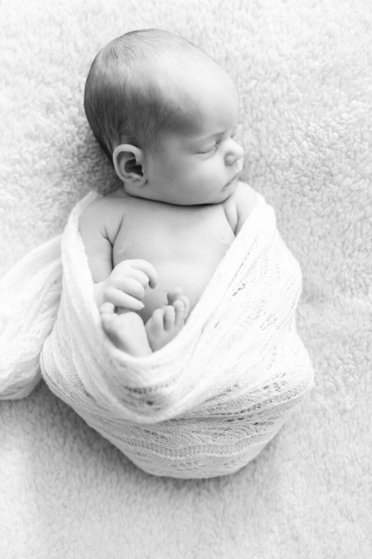 Newborn baby ingepakt in een witte doek, liggend op een zachte ondergrond met de oogjes dicht.
