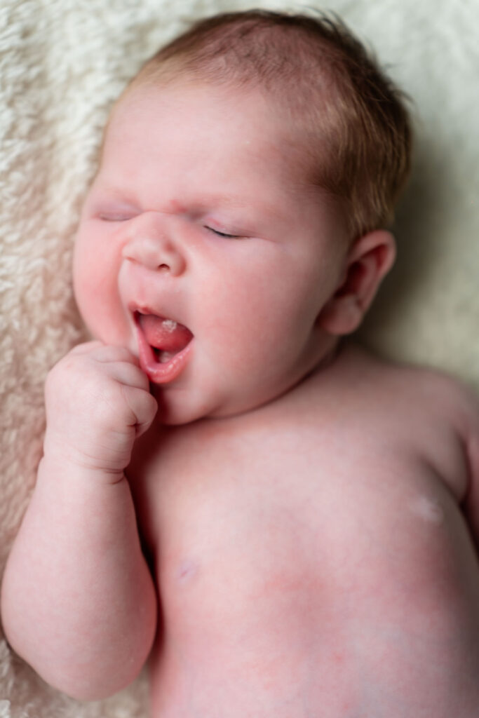 Pasgeboren baby gaapt terwijl zij haar vuistje naar zijn mondje brengt, vastgelegd door newborn fotograaf Daphne