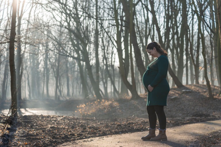 Zwangere vrouw kijkt liefdevol naar haar buik tijdens een shoot zwangerschap in Spijkenisse, omringd door bomen en zacht licht.