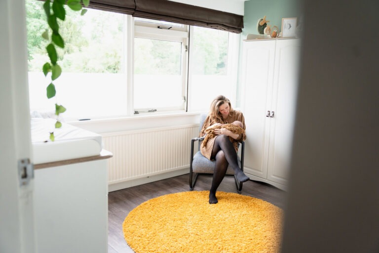 Moeder zit met baby in de babykamer bij het raam Een intiem moment tussen moeder en baby Lucas in hun eigen huis, vastgelegd door een lifestyle newbornfotograaf.