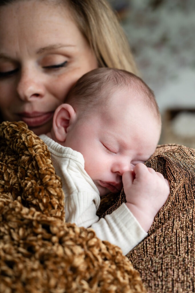 Moeder knuffelt haar slapende baby tegen haar schouder Moeder houdt haar pasgeboren zoon Lucas dicht tegen zich aan tijdens een intiem moment vastgelegd door een newbornfotograaf.