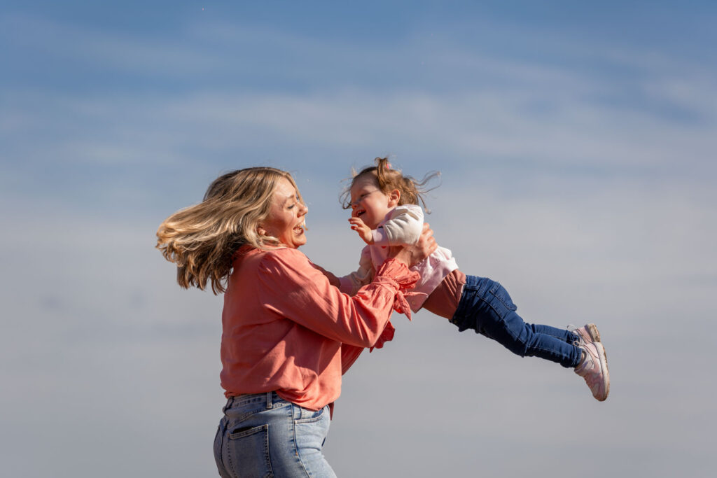 Moeder tilt dochter op in de tulpenvelden – Moeder en dochter lachen samen tijdens een speels moment in het tulpenveld in Oudenhoorn.