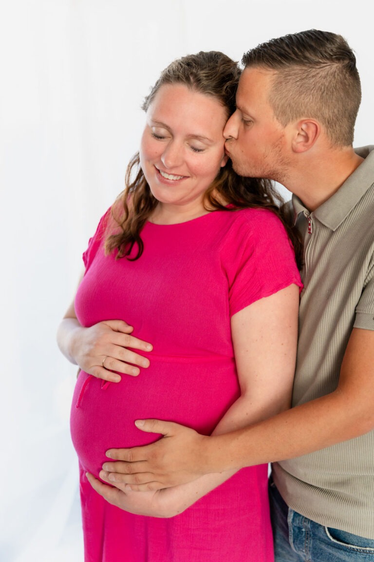 wangere vrouw krijgt een kus van haar partner tijdens zwangerschapsfotografie in de studio