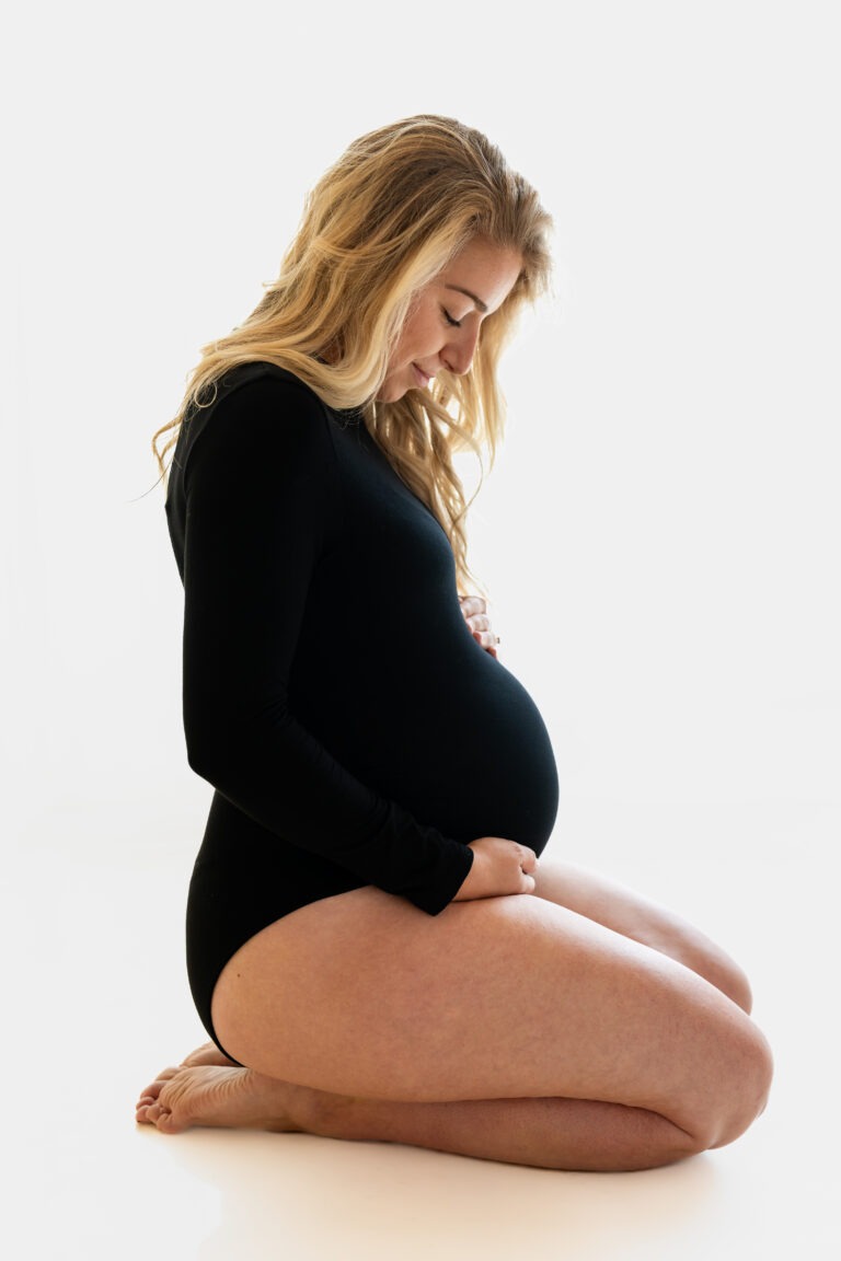 Zwangerschapsshoot in zwarte body – knielend in de daglichtstudio met rustige uitstraling