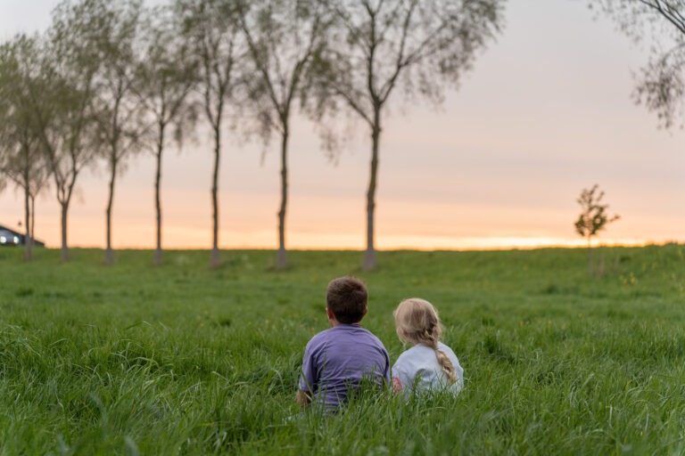Twee kinderen zitten samen in het hoge gras tijdens familiefoto buiten in Zuidland