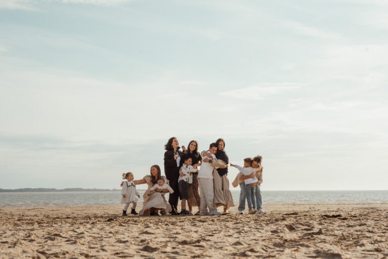 Samengestelde familie poseert met kinderen aan zee tijdens een ontspannen strandshoot