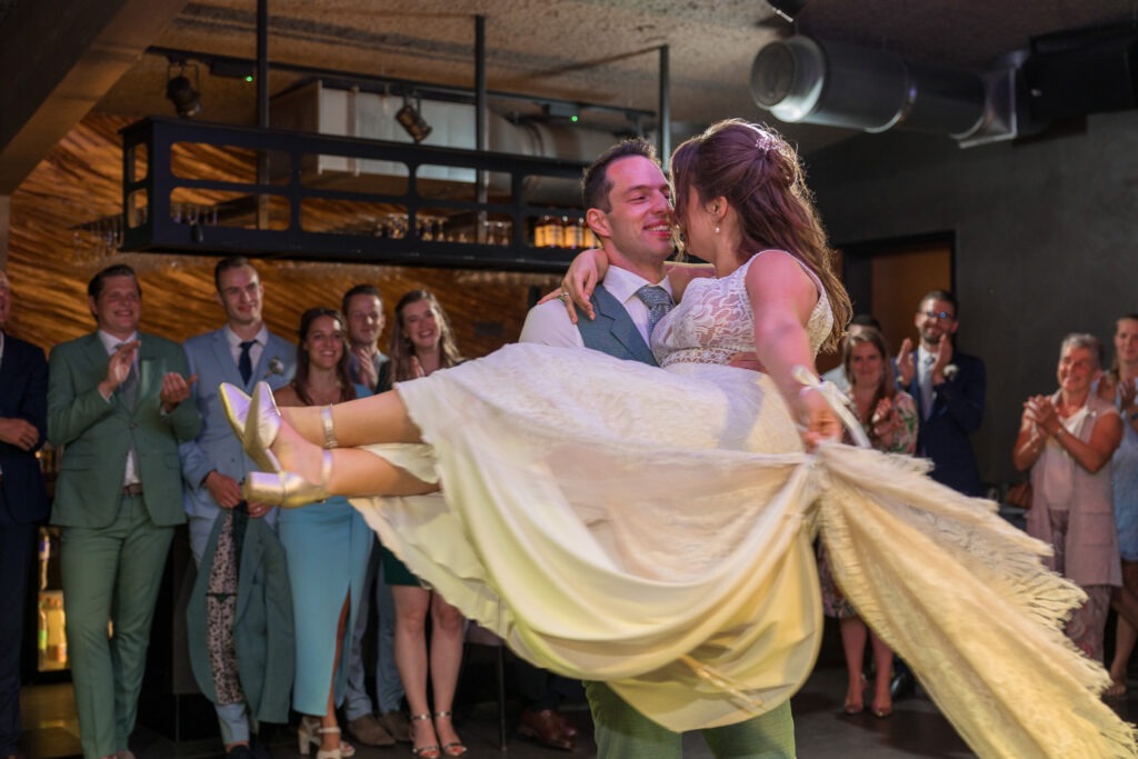 Bruidegom tilt zijn bruid op tijdens hun openingsdans Tijdens het feest tilt de bruidegom zijn bruid vol trots op, terwijl de gasten klappen en glimlachen – een stralende start van de dansvloer.