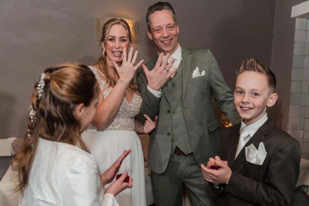 Vers getrouwd stel toont trots hun ringen aan hun kinderen De bruid en bruidegom lachen breed terwijl ze hun handen omhoog houden om hun trouwringen te laten zien aan hun kinderen.