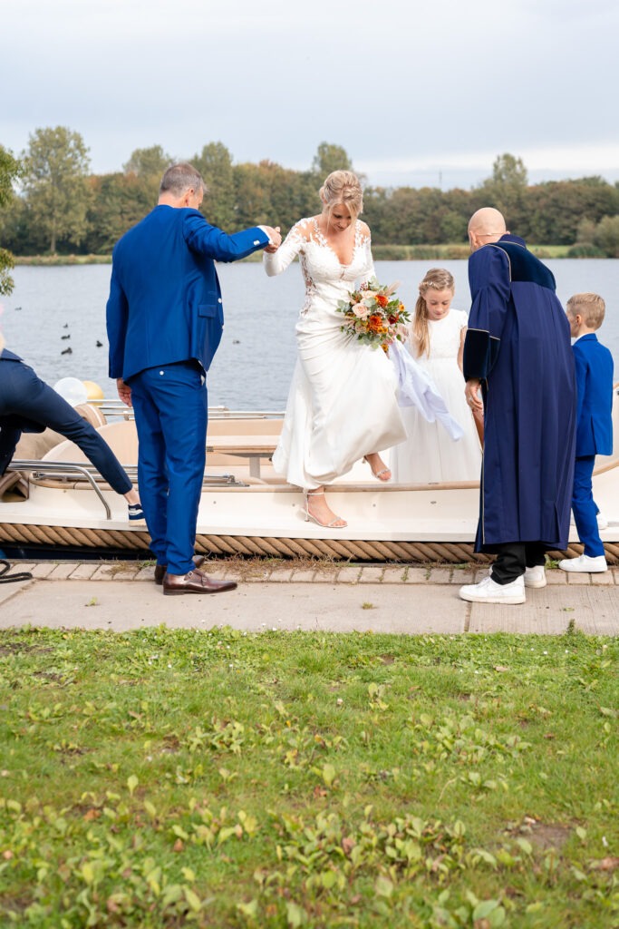 Bruid stapt met hulp van bruidegom van de boot De bruidegom helpt zijn bruid voorzichtig van de boot terwijl ze haar jurk optilt en haar boeket stevig vasthoudt.