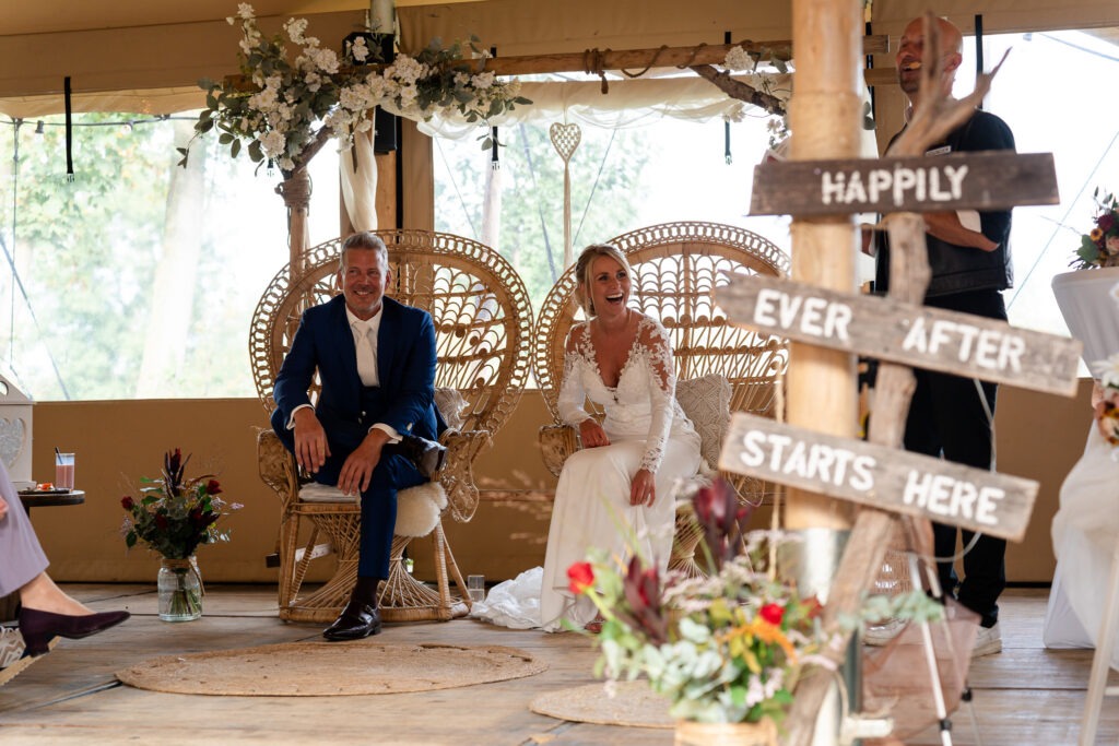 Bruidspaar lacht samen tijdens de ceremonie De bruid en bruidegom schieten in de lach tijdens een grappige opmerking van de trouwambtenaar, terwijl de gasten meegenieten.