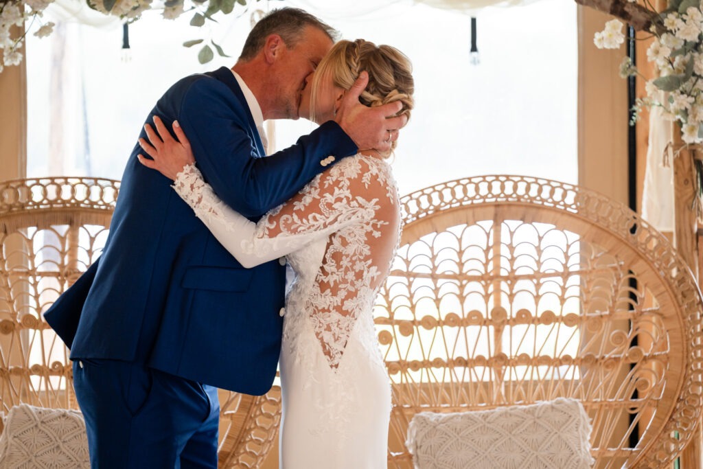 Eerste kus van het bruidspaar na het jawoord Het bruidspaar kust elkaar voor het eerst als man en vrouw, met hun handen stevig om elkaar heen – een warm en intiem moment.