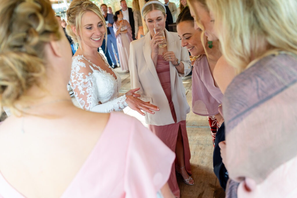 Bruid toont haar ring aan vriendinnen tijdens de borrel De bruid laat lachend haar trouwring zien aan haar vriendinnen, die nieuwsgierig om haar heen staan tijdens het feest.