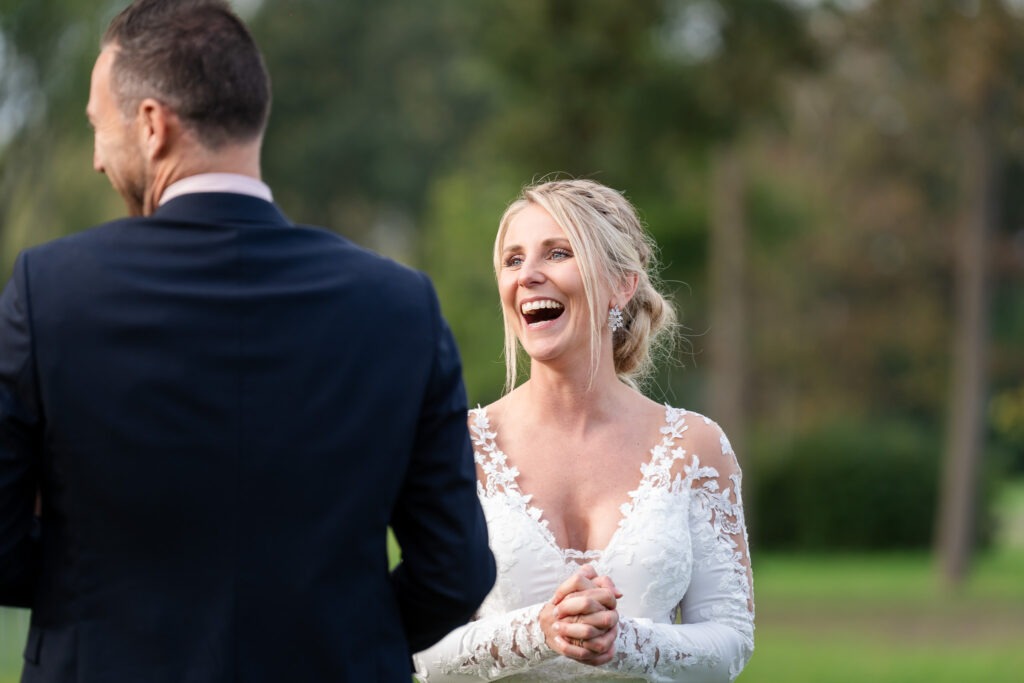 Bruid lacht uitbundig tijdens een gesprek buiten De bruid in haar kanten jurk schiet in de lach tijdens een gesprek met een van de gasten in de tuin van de trouwlocatie.