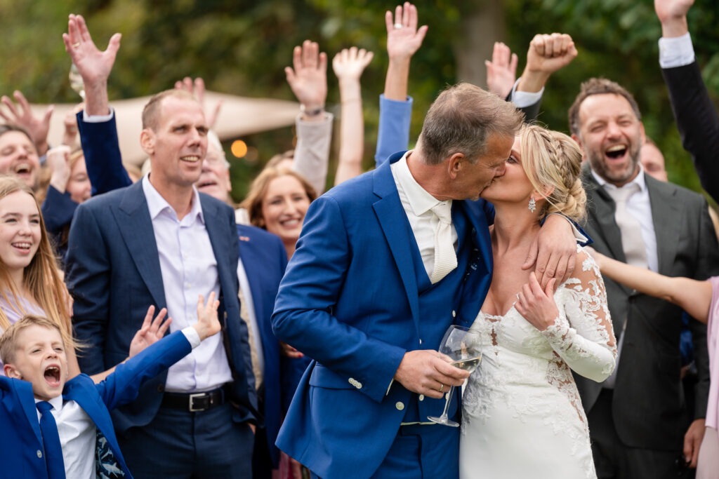 Bruidspaar kust elkaar tussen juichende gasten Het bruidspaar deelt een kus terwijl familie en vrienden om hen heen juichen — pure feestvreugde gevangen in één beeld.