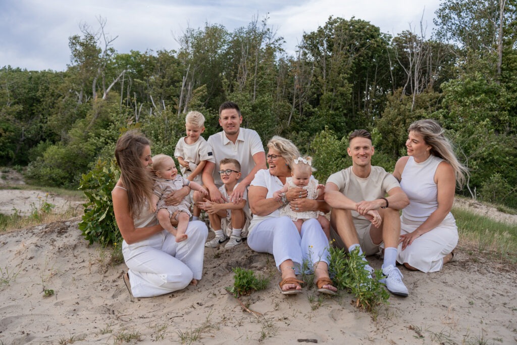 Grote familiefoto in de duinen van Rockanje Drie generaties bij elkaar tijdens een familieshoot in Rockanje – zittend in het zand, omringd door groen en gekleed in neutrale tinten. Een warme en vrolijke groepsfoto vol echte momenten.