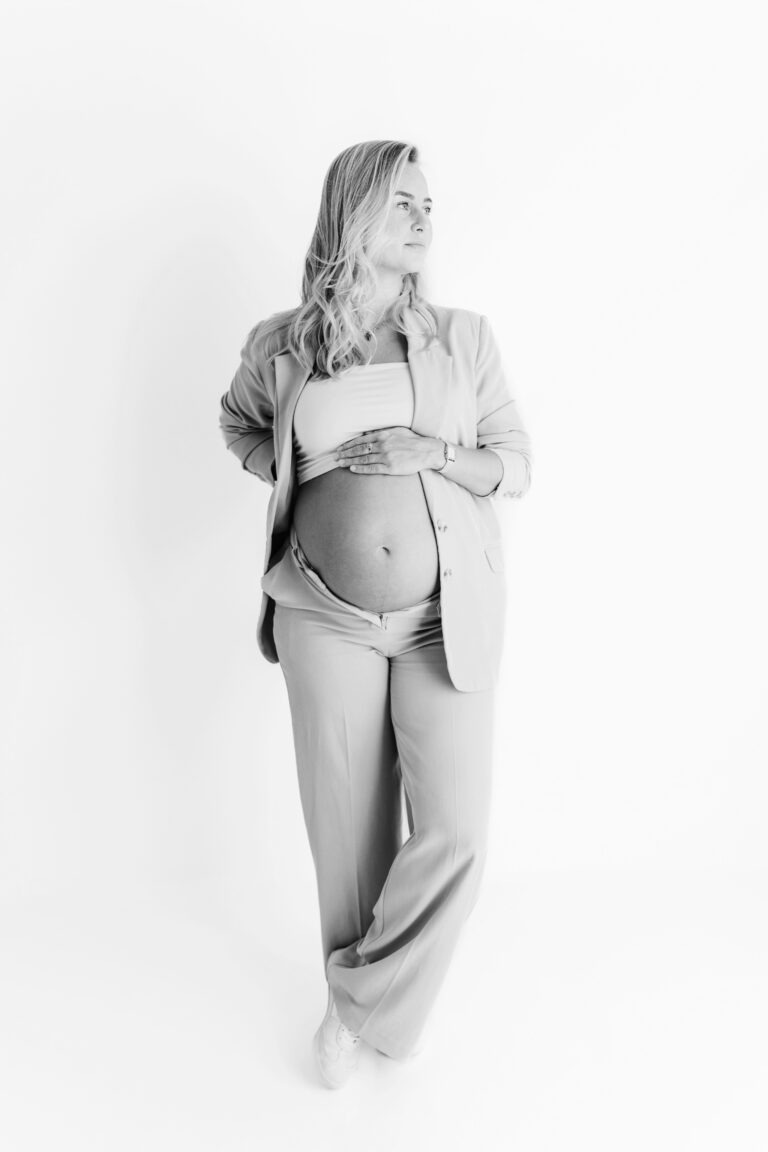 Zwangere vrouw in stijlvol beige pak poseert tijdens zwangerschapsfotografie in Daphne's Fotografie studio.
