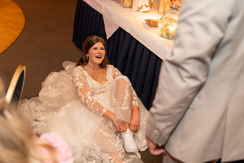 Bruid zit lachend op de grond terwijl de bruidegom haar helpt tijdens een spontaan moment