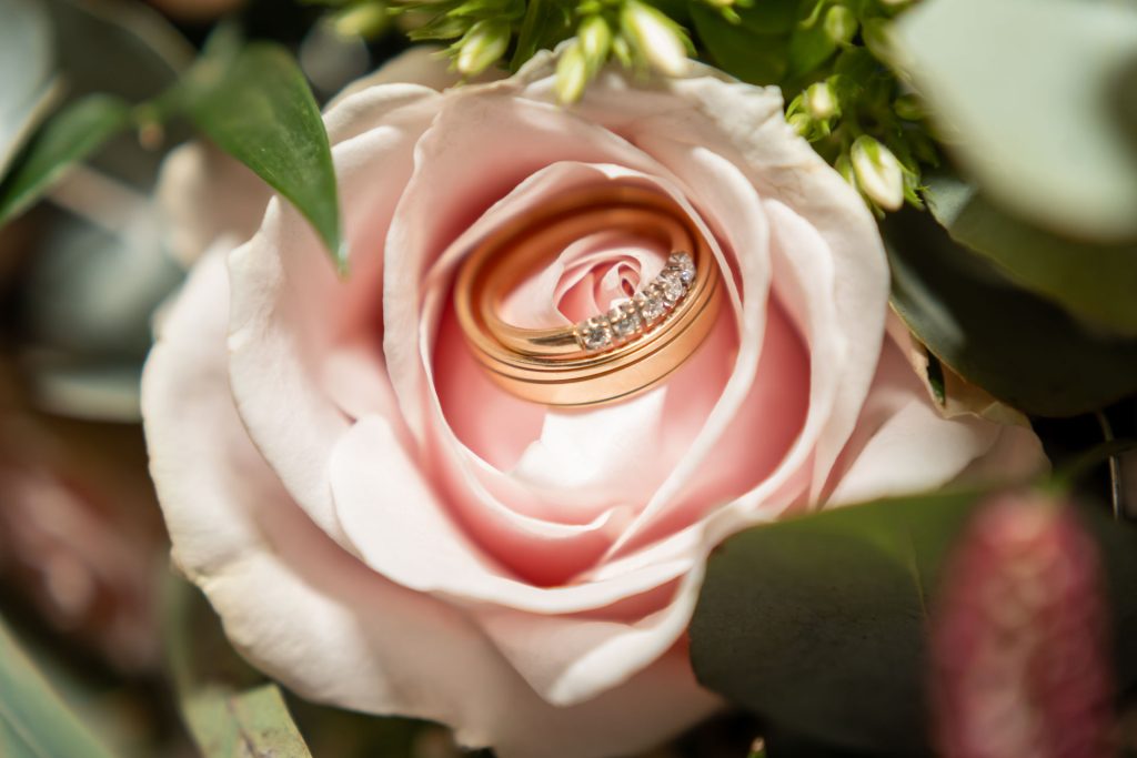 Detailfoto van trouwringen in een zachte roze roos