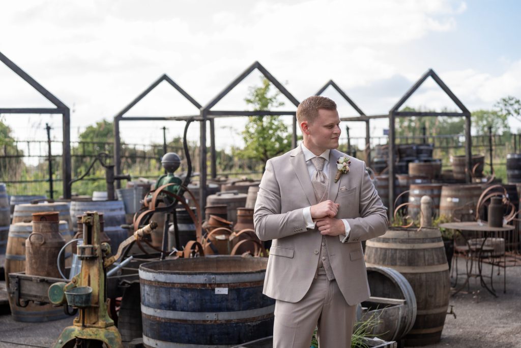 Bruidegom staat ontspannen te wachten tussen houten vaten op de trouwlocatie