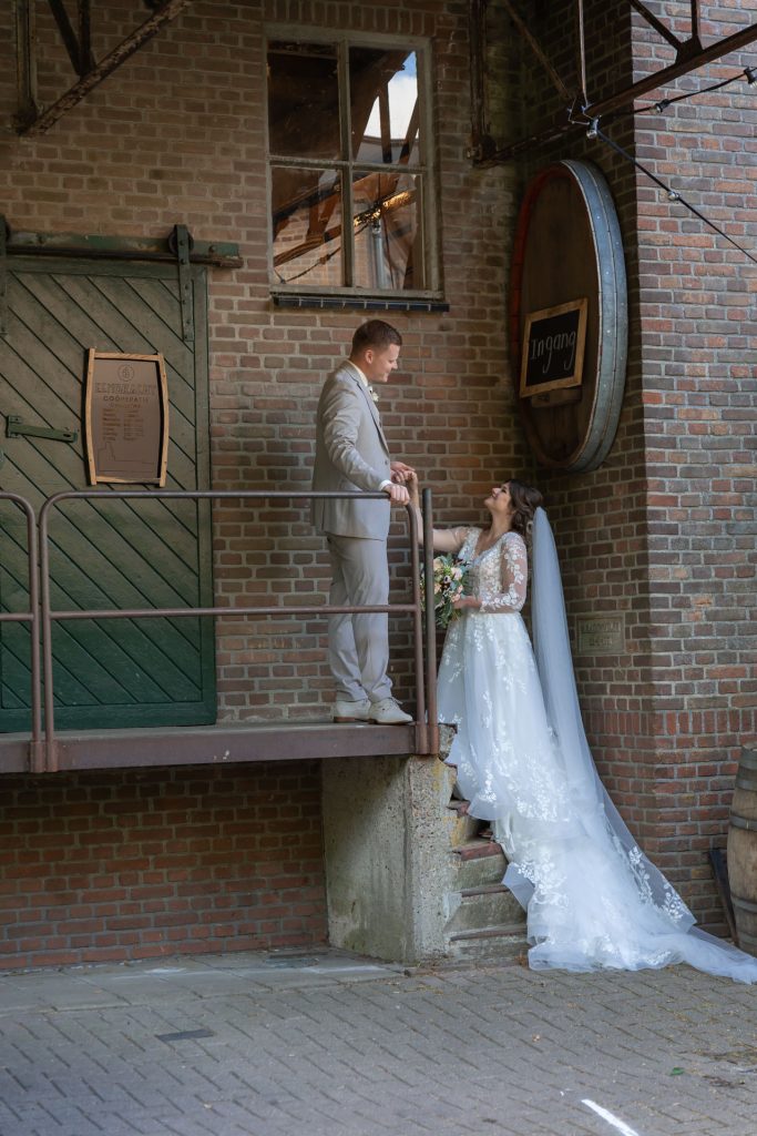 Bruid en bruidegom staan samen op een trap bij een oude suikerfabriek