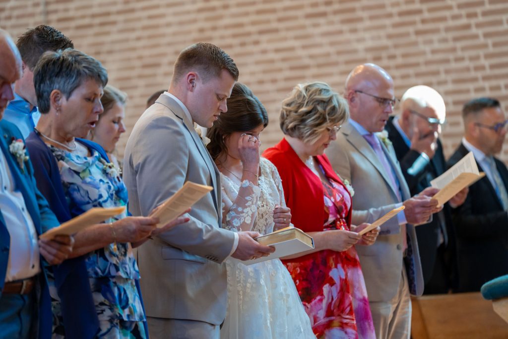 Bruid en gasten lezen mee tijdens een emotioneel moment in de huwelijksceremonie