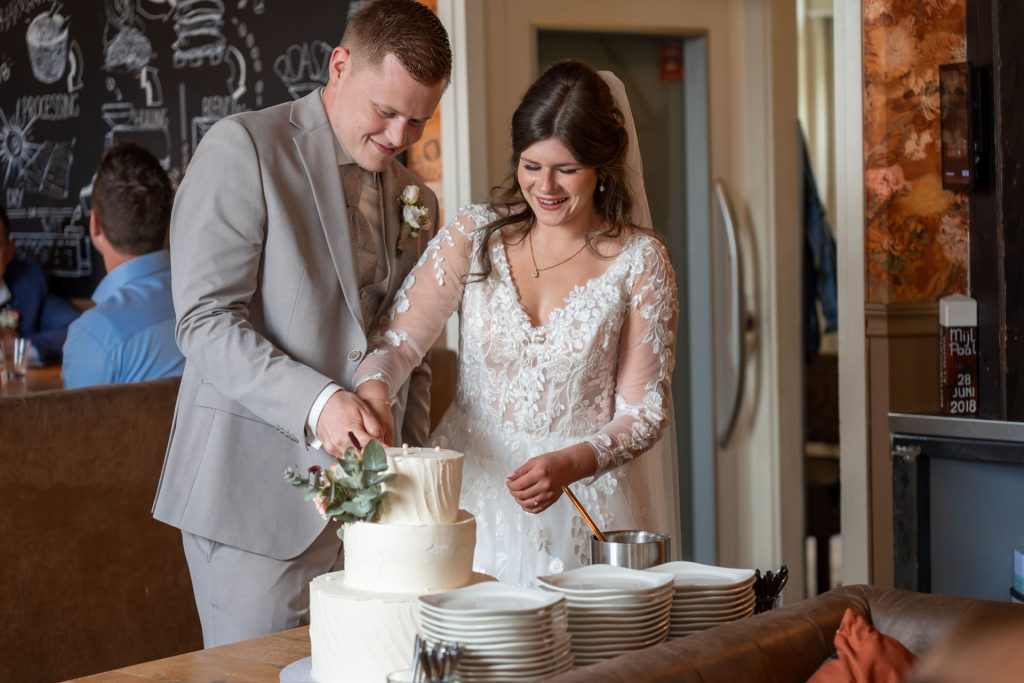 Bruid en bruidegom snijden samen de bruidstaart aan tijdens de receptie