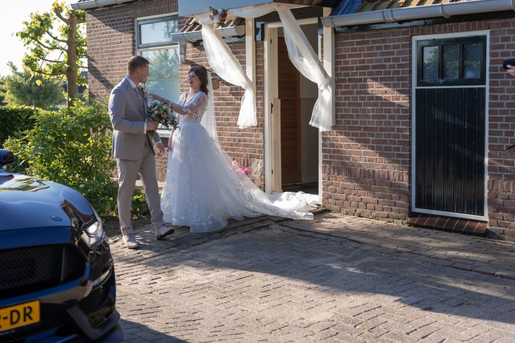 Bruid en bruidegom lachen samen voor de voordeur van hun trouwlocatie